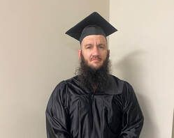 A man with a beard dressed in a graduation cap and gown