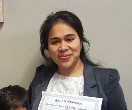 A woman with dark hair who is dressed professionally and holding a certificate