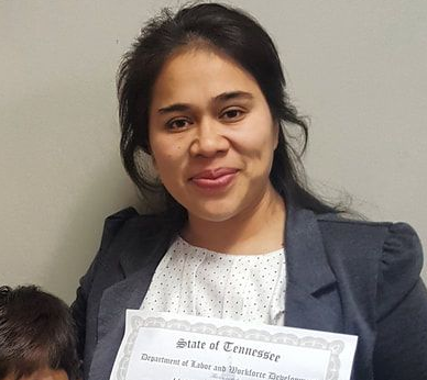 One of the participants of adult education, wearing a black and white blazer and holding a certificate