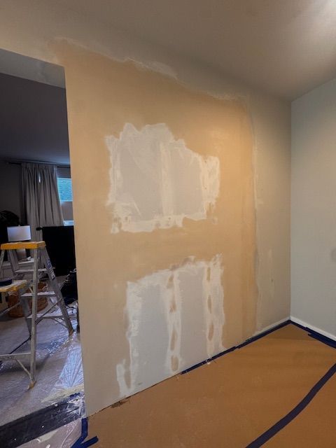 Wall under construction, with visible drywall patches and joint compound, ready for paint.