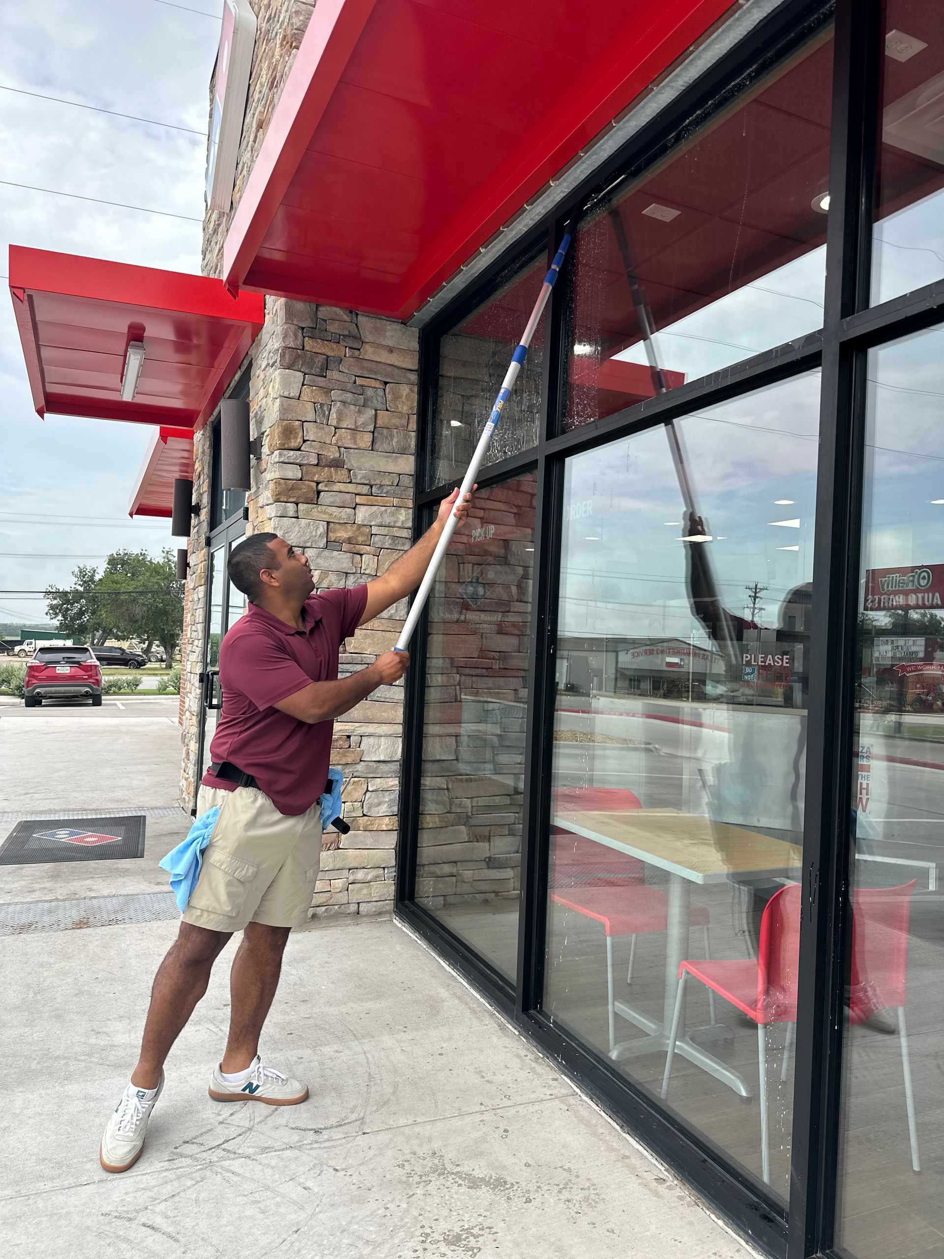 A man is cleaning the windows of a restaurant with a mop.