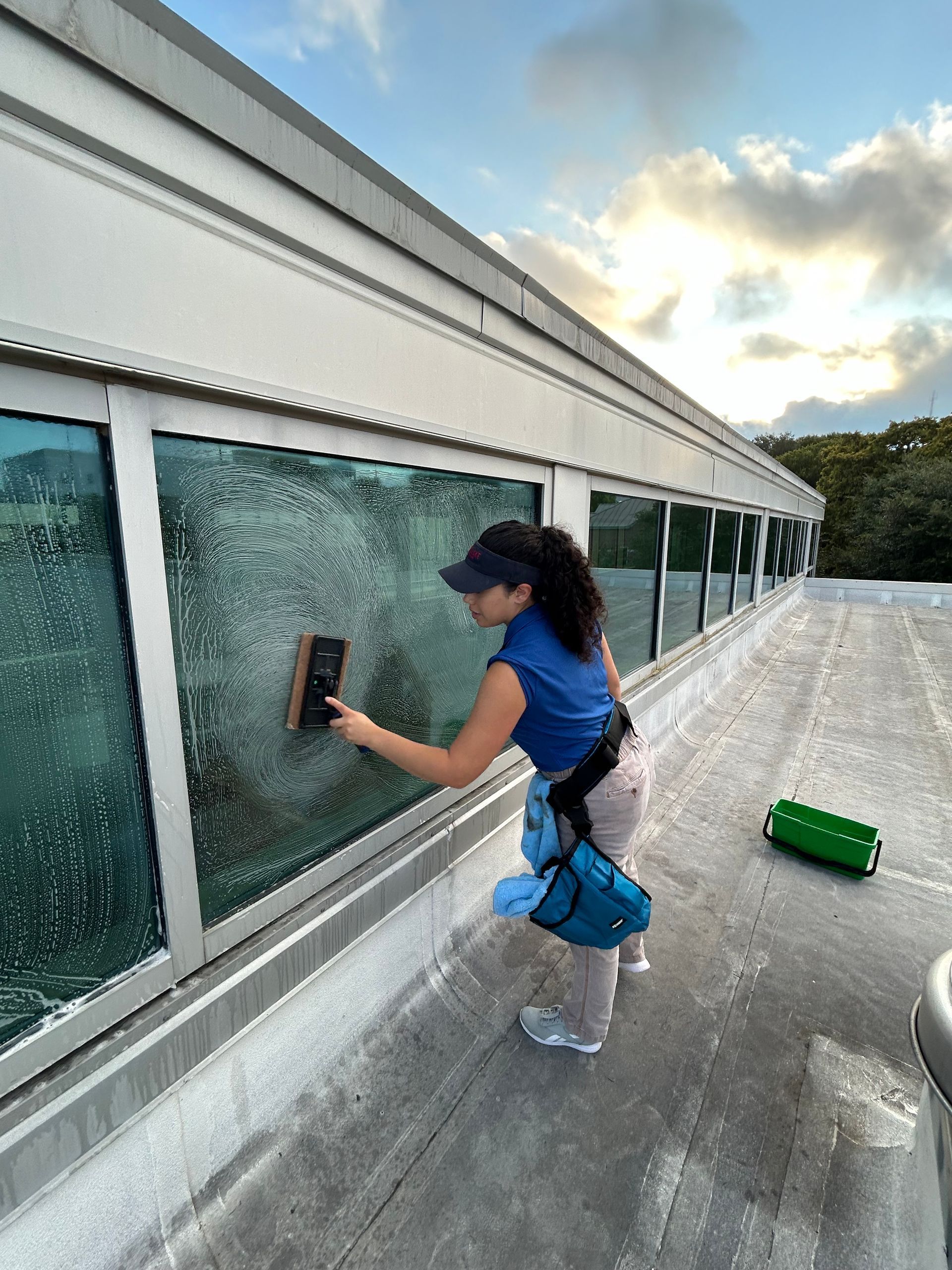 A woman is cleaning a window on the roof of a building.