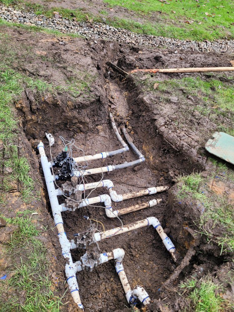 PVC pipes and valves laid in a trench beside a grassy yard during plumbing work