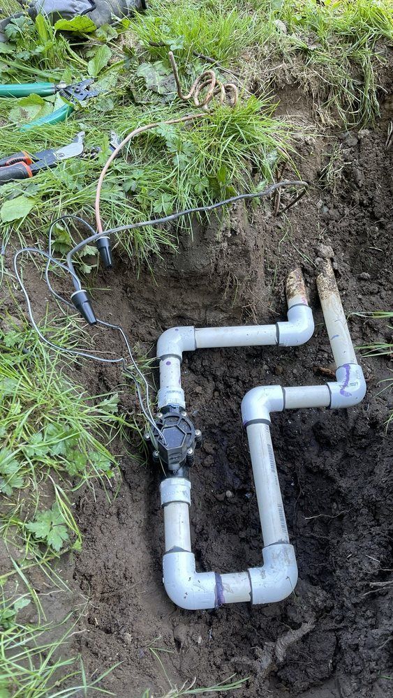 PVC pipes laid in a dirt trench beside grass, with a blue cable running above them
