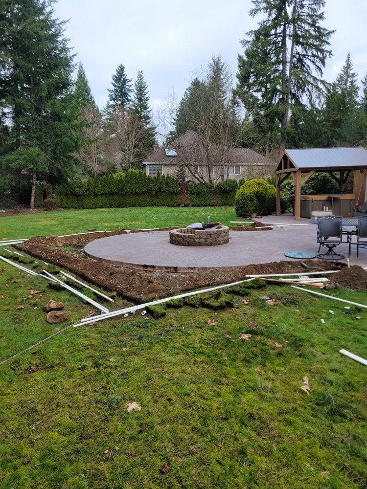 Backyard patio with circular stone fire pit, wooden gazebo, and evergreen trees after rain
