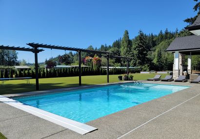 Backyard swimming pool with clear blue water, bordered by brick and surrounded by green lawn and trees