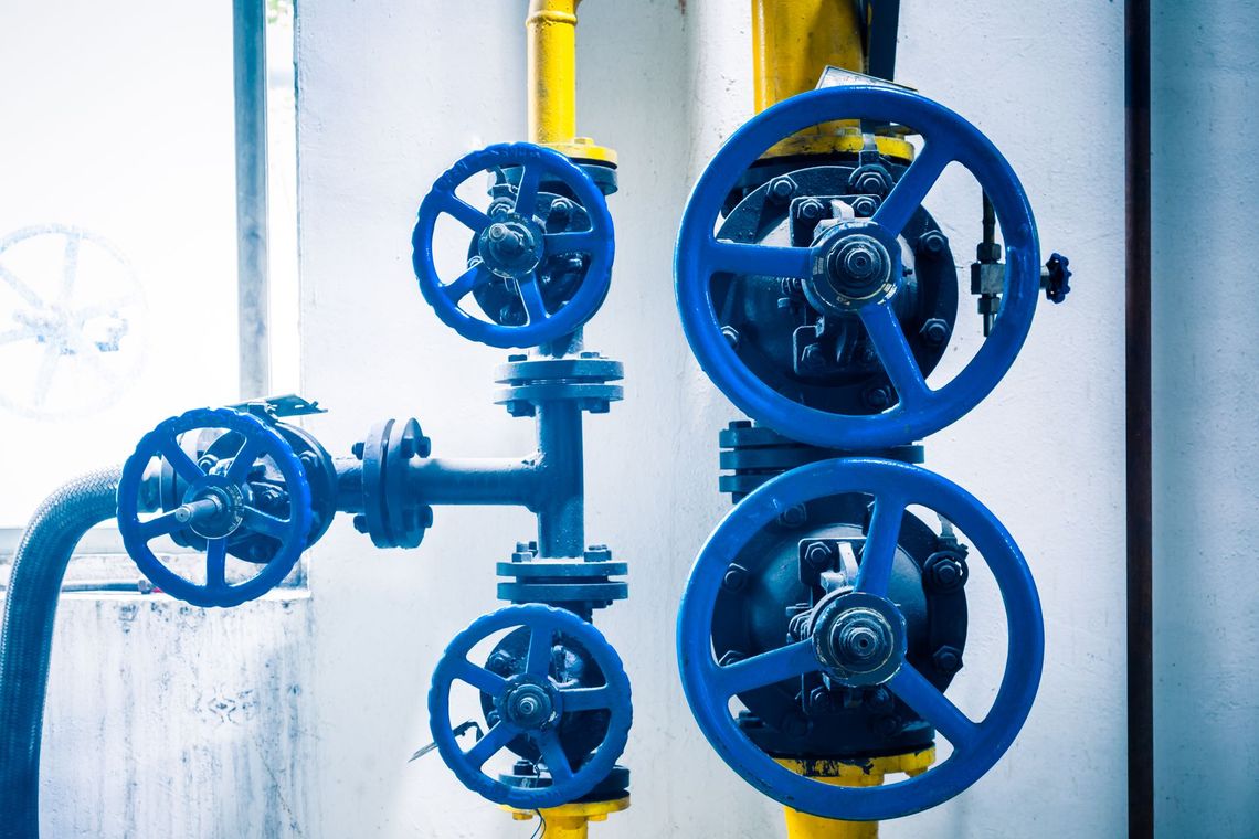 Blue industrial pipe valves with yellow piping against a white wall