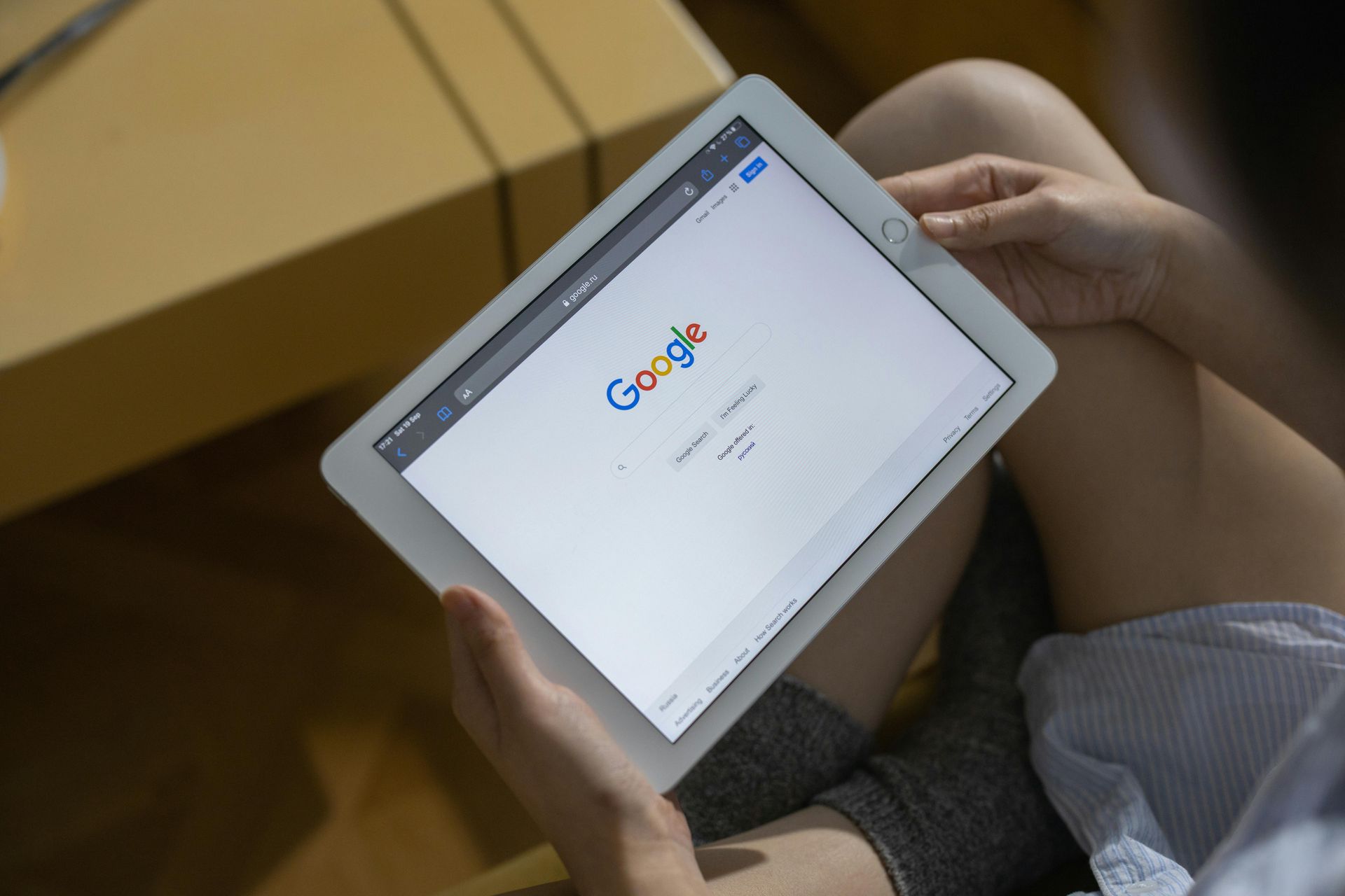 Person using a tablet displaying the Google search page; indoors.