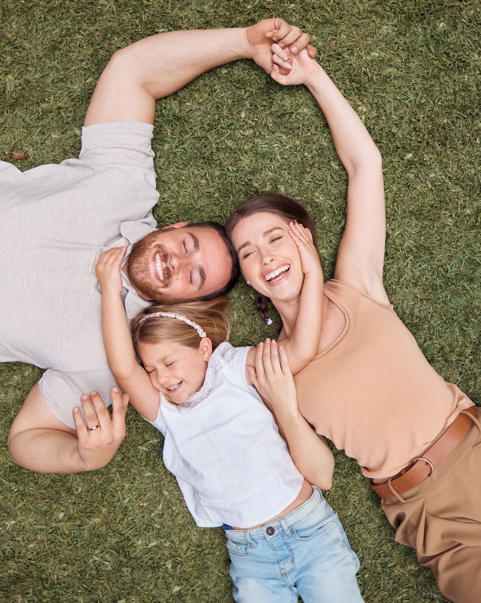 A family is laying on the grass making a heart shape with their hands.