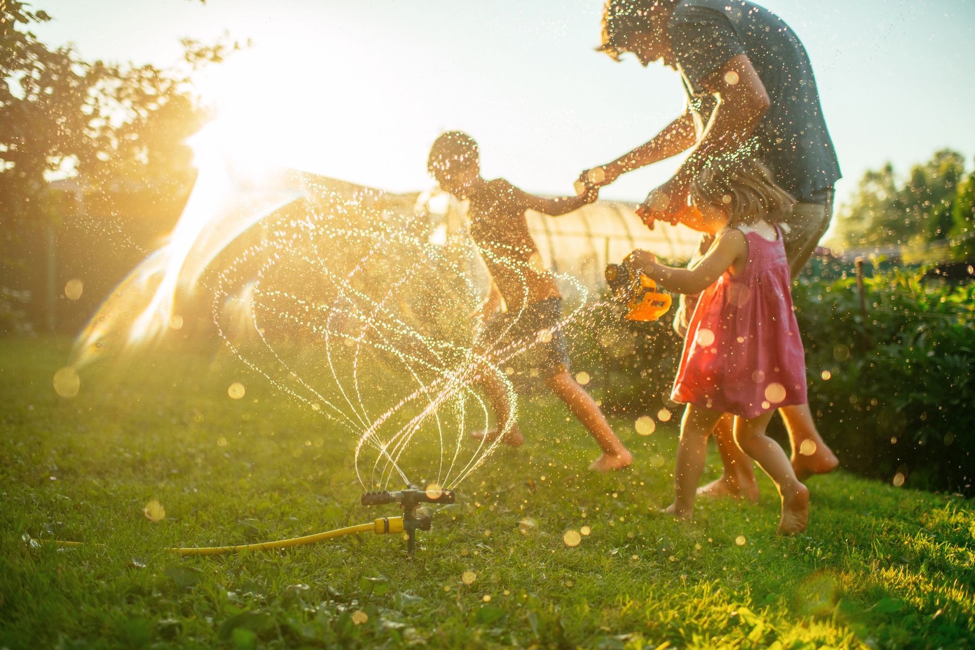 A family is playing with a sprinkler in their backyard.