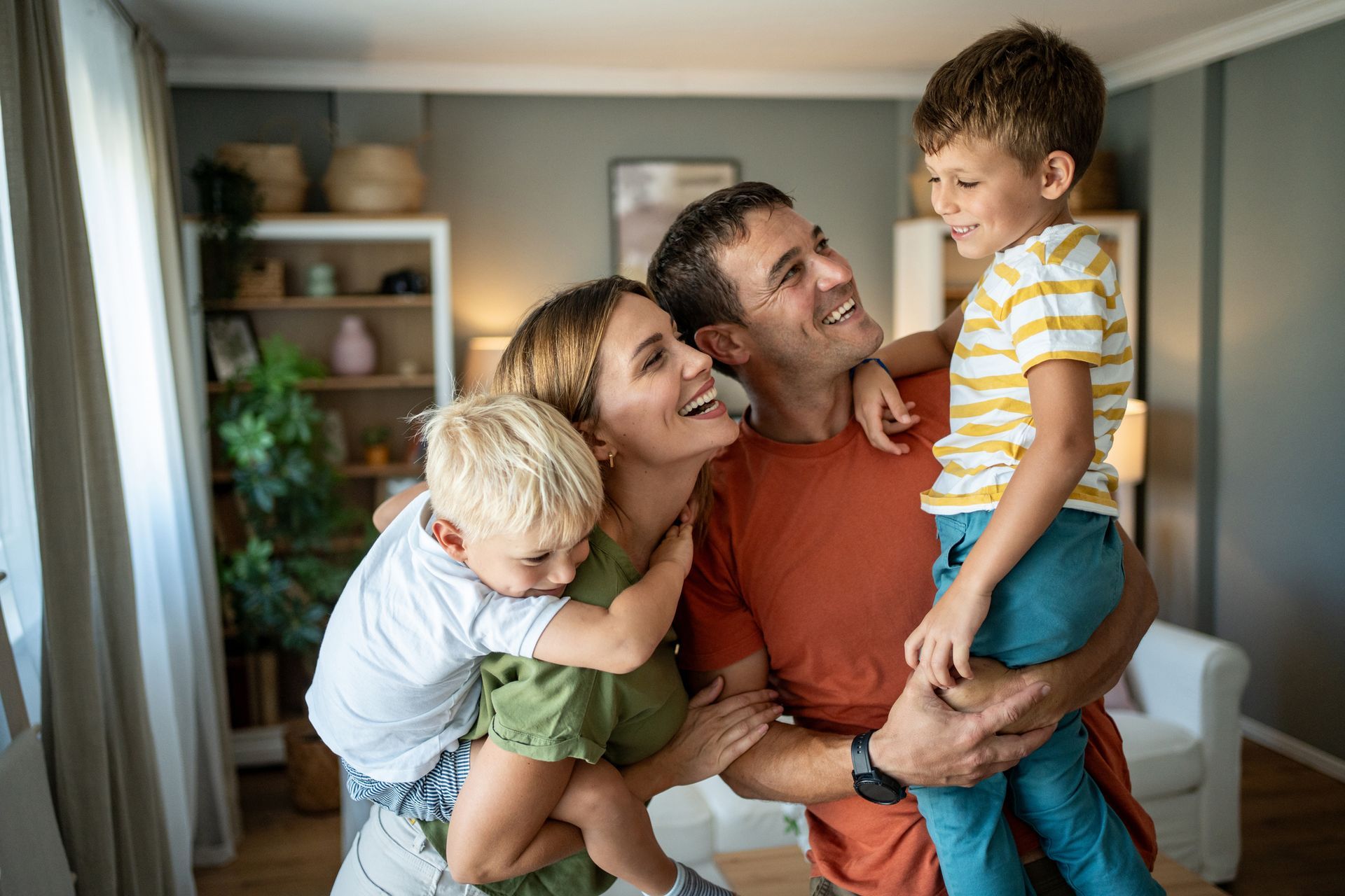 A family is standing in a living room holding two children.