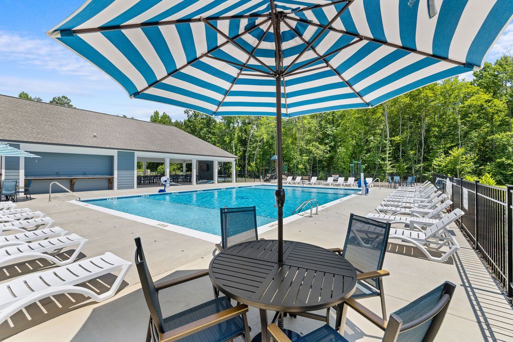 A table and chairs under an umbrella next to a swimming pool.