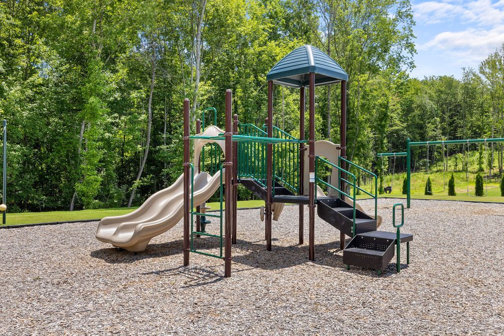 A playground with a slide , swings , and stairs in a park.