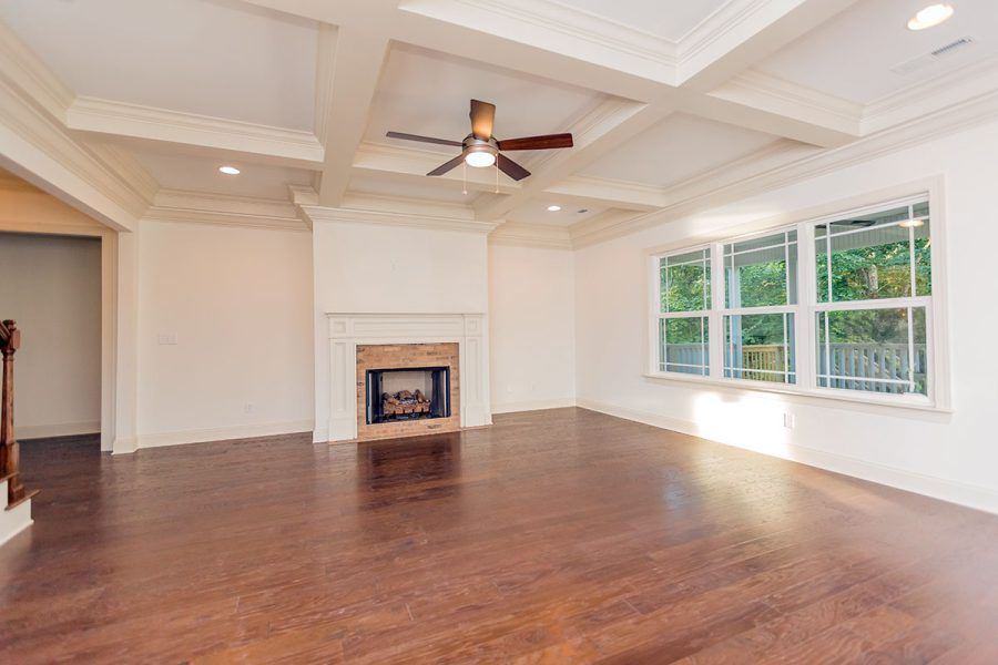 An empty living room with hardwood floors , a fireplace and a ceiling fan.