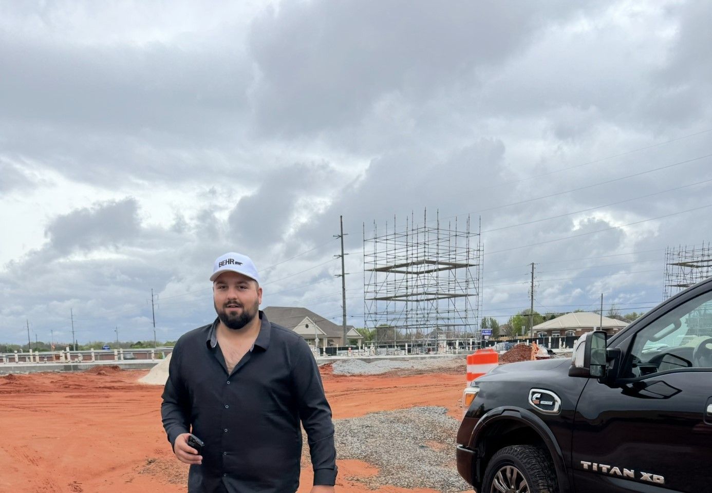A man is standing next to a black truck in a dirt field.