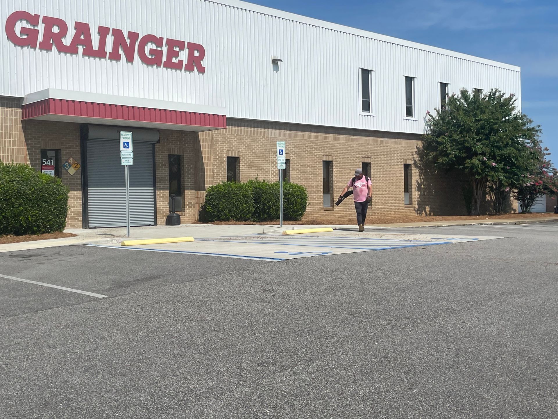 A person in a pink shirt is leaf blowing in front of a building that says grainer.