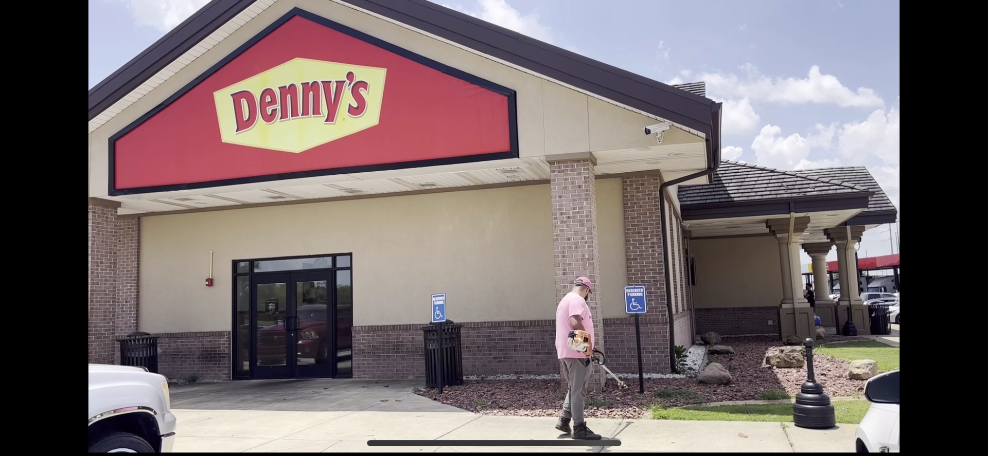 A man is weed eating in front of a denny's restaurant.