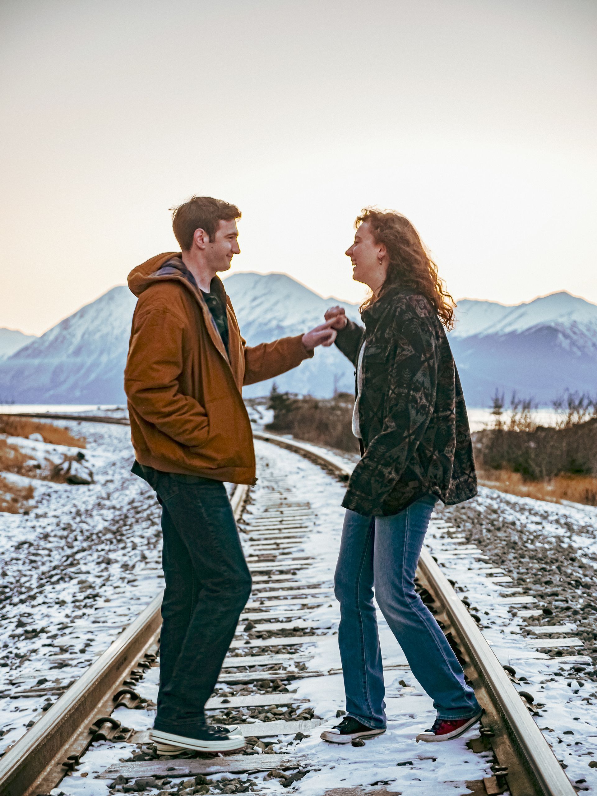 A man and a woman are standing on train tracks in the snow.