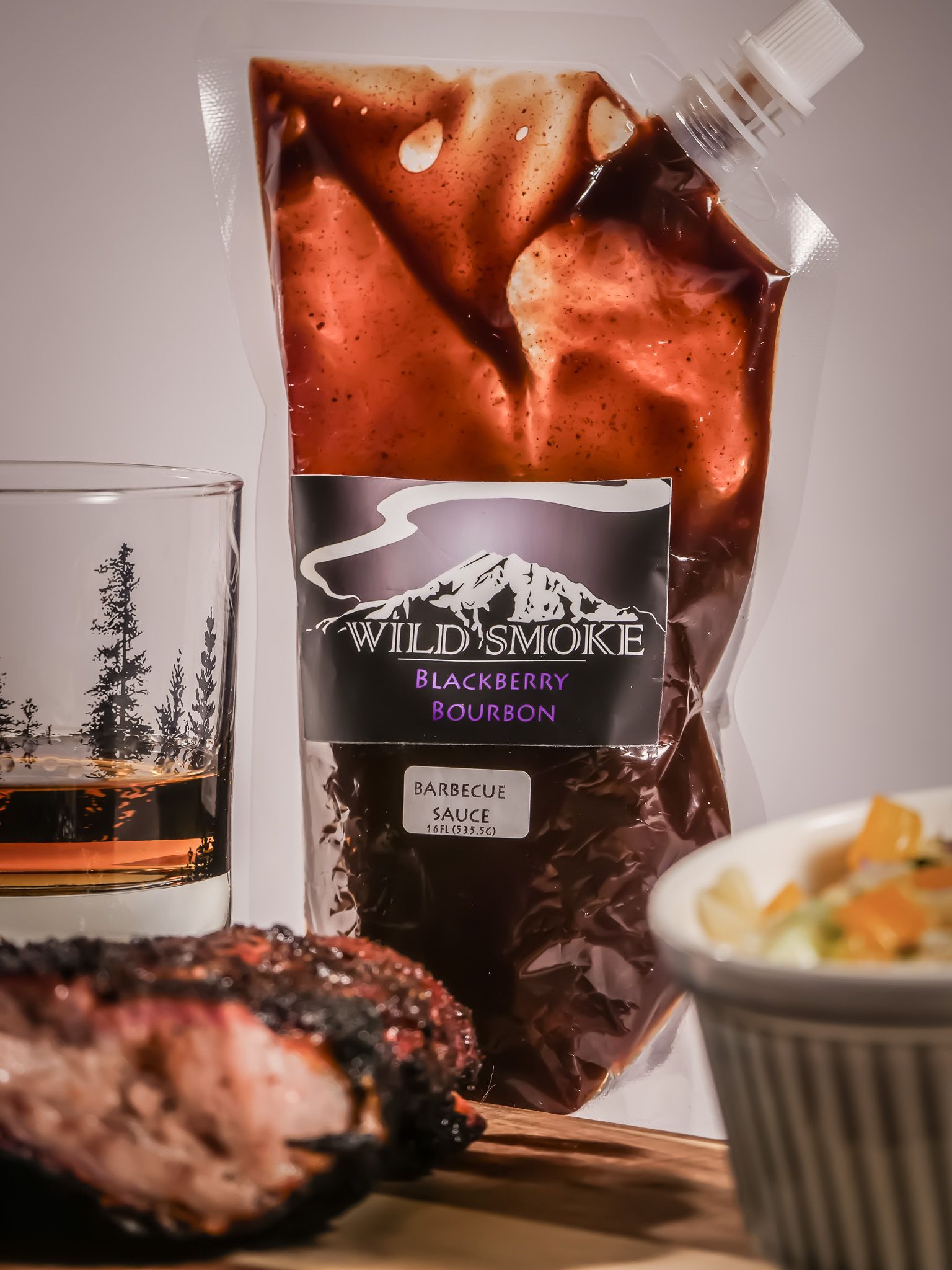 A bag of wild smoke barbecue sauce next to a glass of whiskey