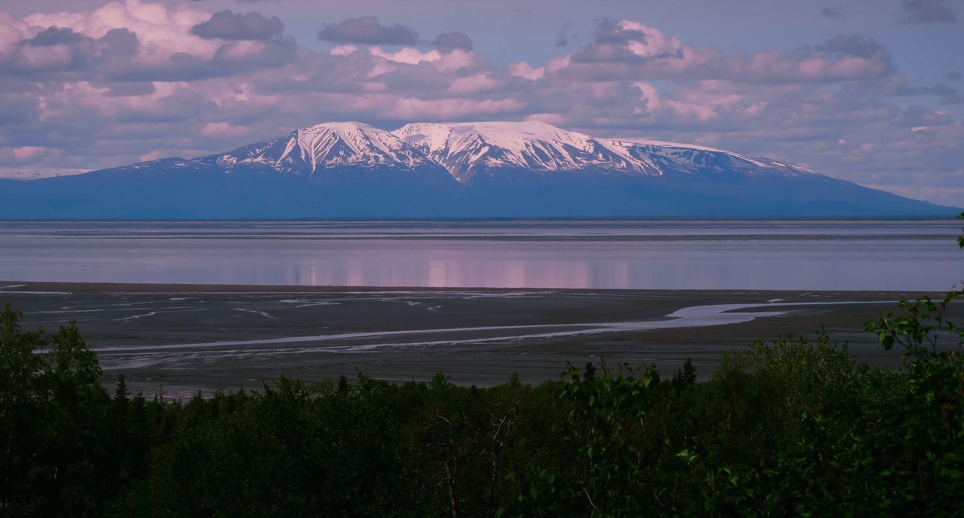 A white car is parked on a dirt road with mountains in the background