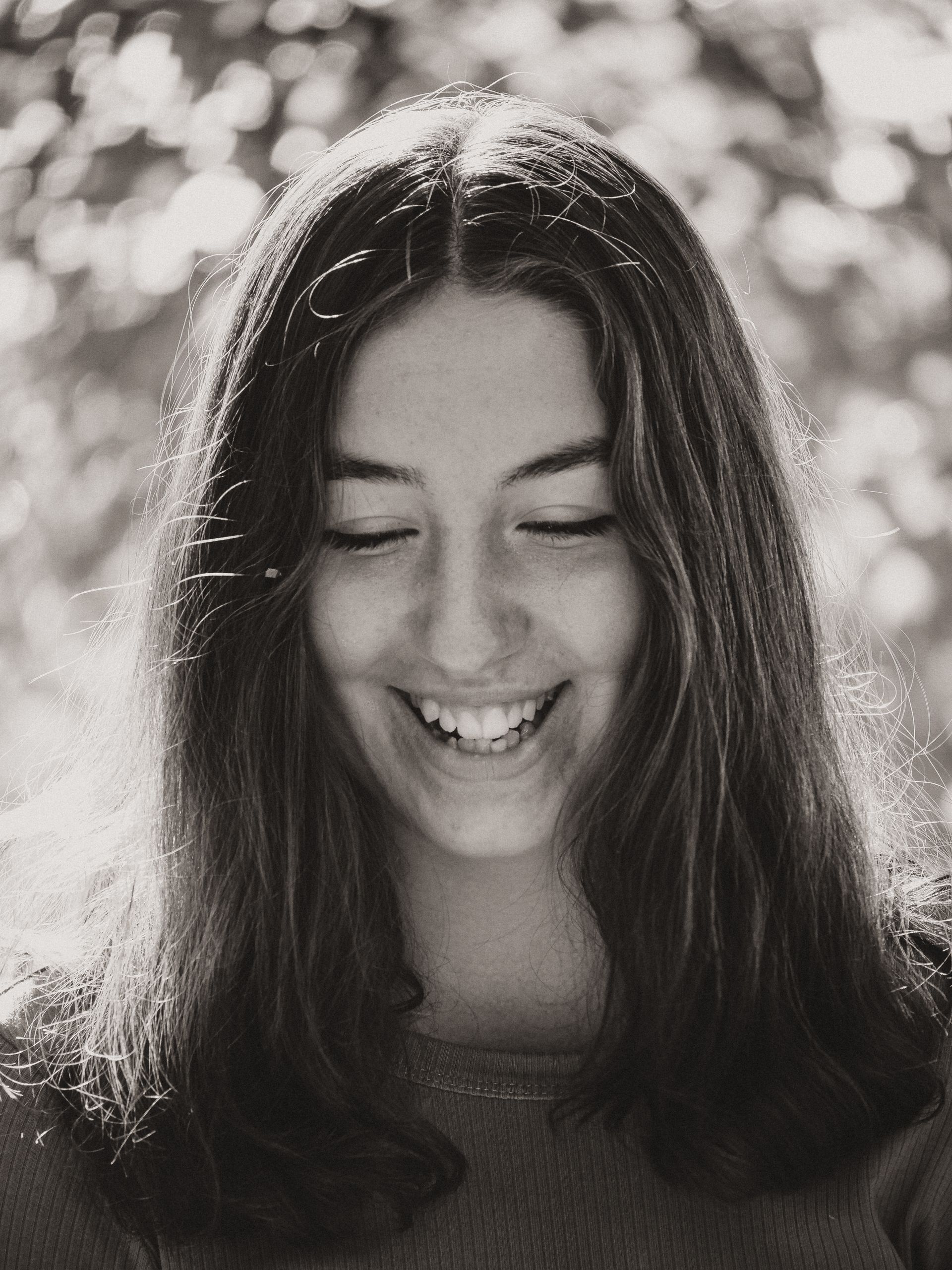 Smiling woman with long hair, eyes closed, outdoors. Black and white portrait.