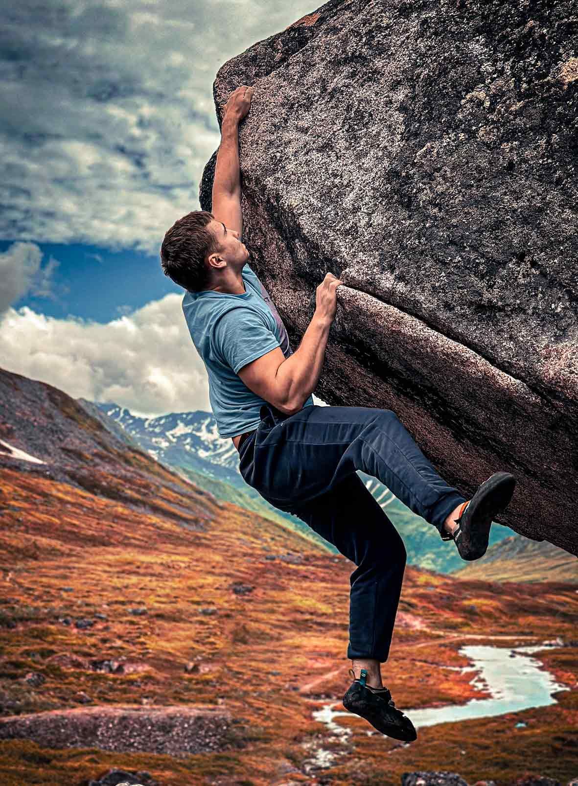 A man is climbing a large rock in the mountains.