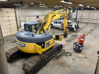 A yellow excavator is parked in a garage next to a truck.