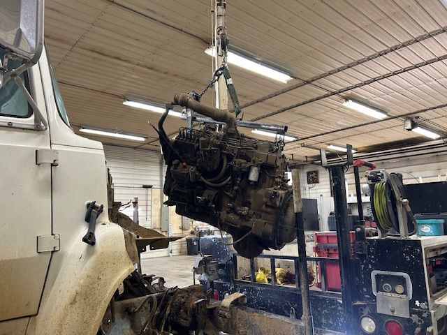 A truck engine is being lifted by a crane in a garage.