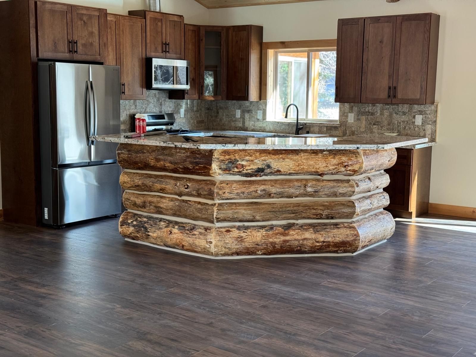 Kitchen with log-style island, granite countertop, stainless steel refrigerator, and dark wood cabinets.