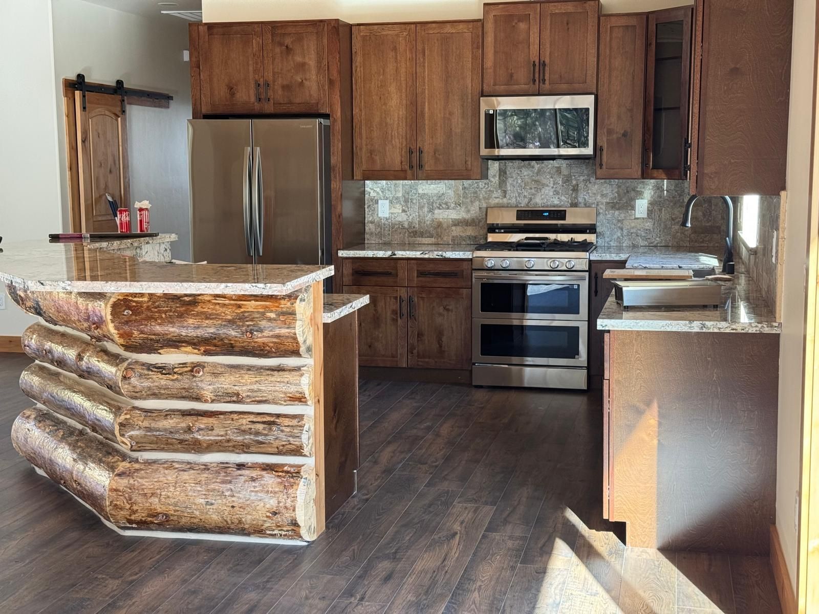 Rustic kitchen with log-style island, stainless steel appliances, wood cabinets, and granite countertops.