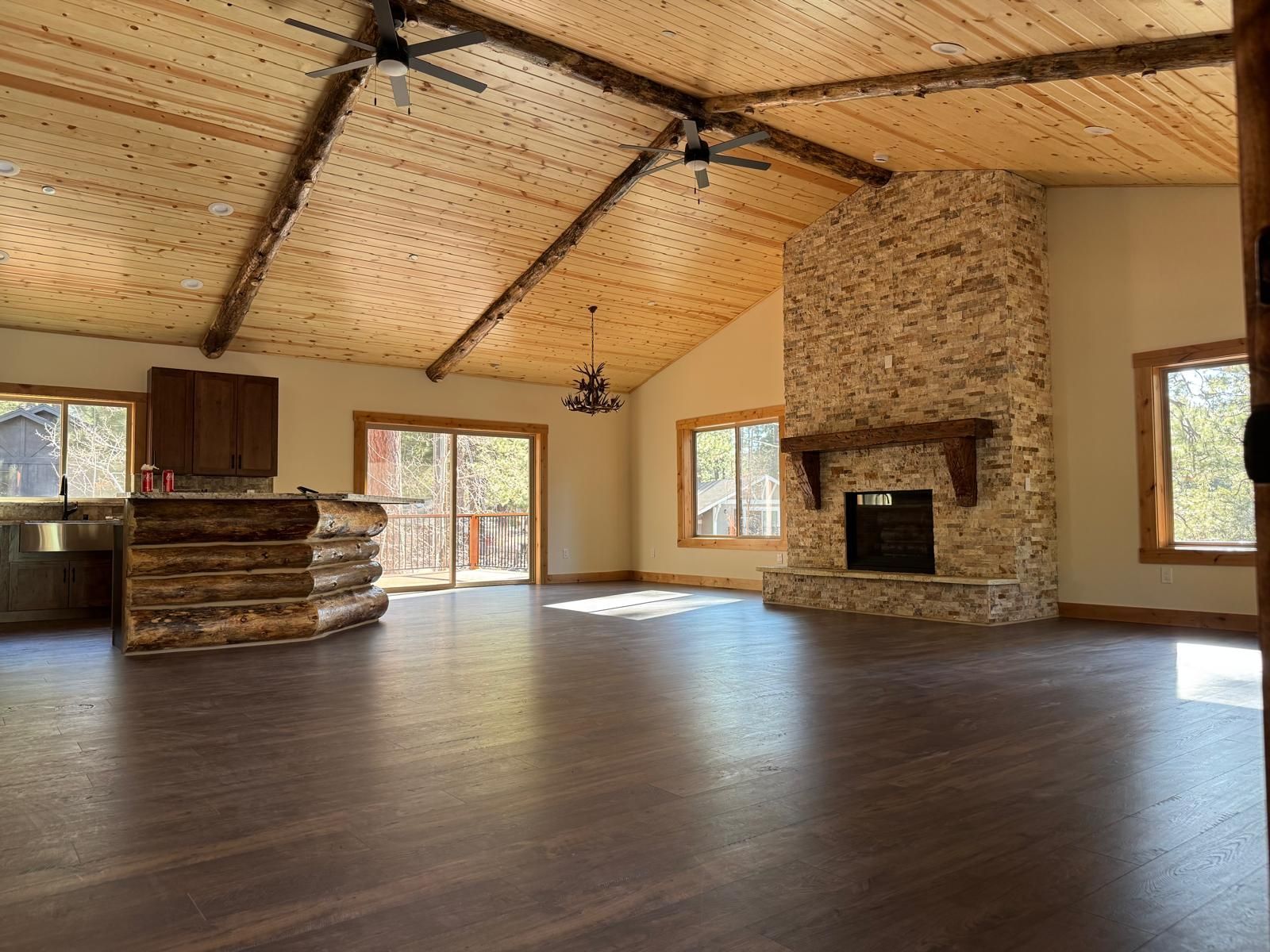 Spacious living room with wood ceiling, stone fireplace, and dark wood floors.