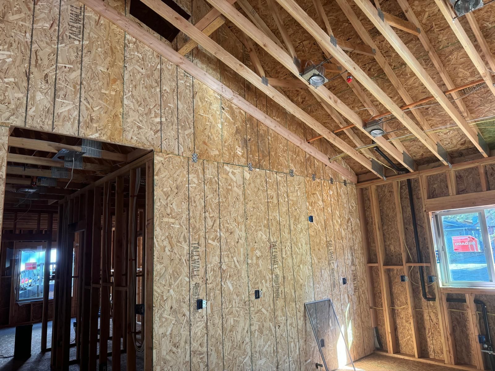 Interior of a building under construction, showing wooden framing and OSB sheathing for walls and ceiling.