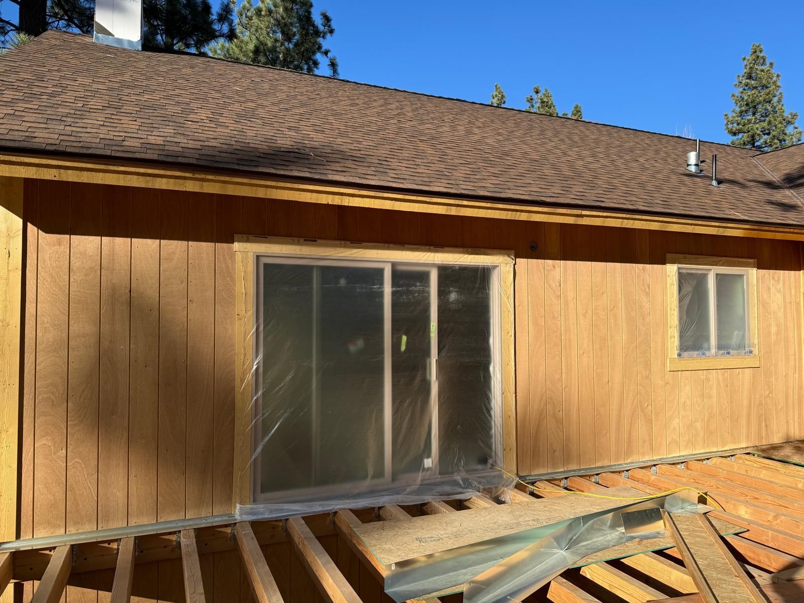 A wooden house with a brown roof and siding, a sliding glass door, and a small window.