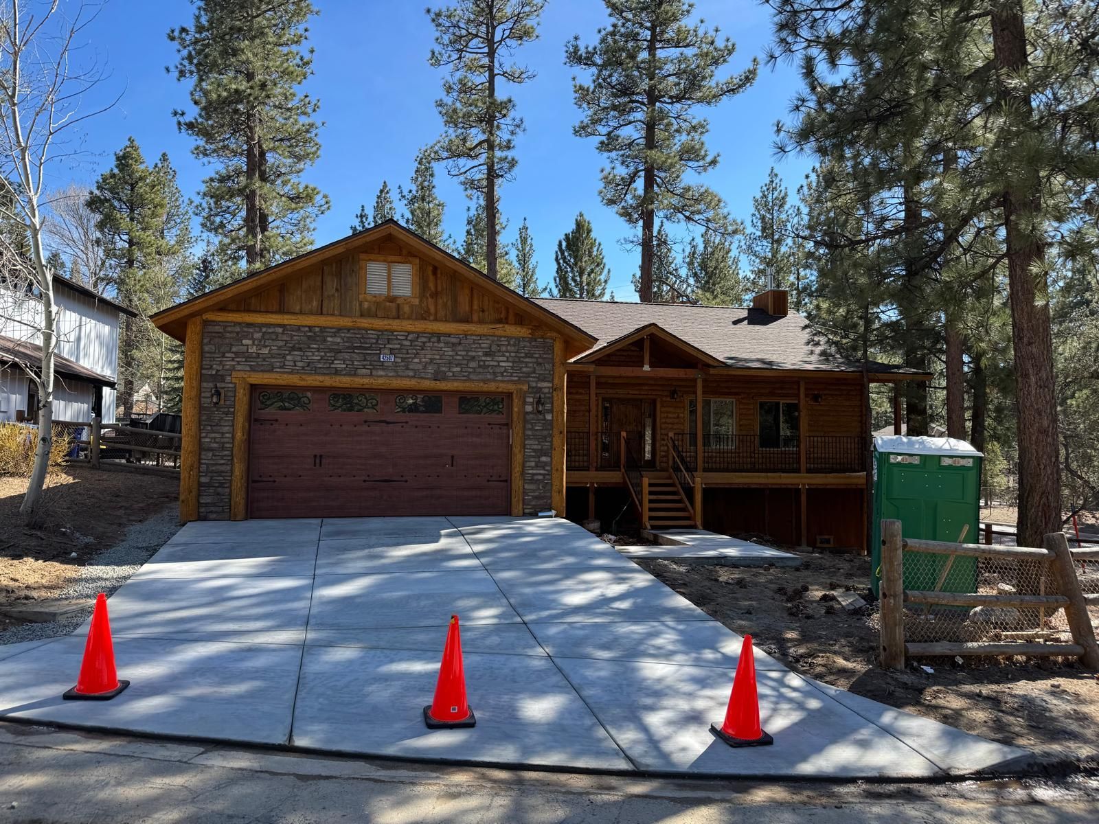 A cabin-style house and garage with a concrete driveway and orange traffic cones.
