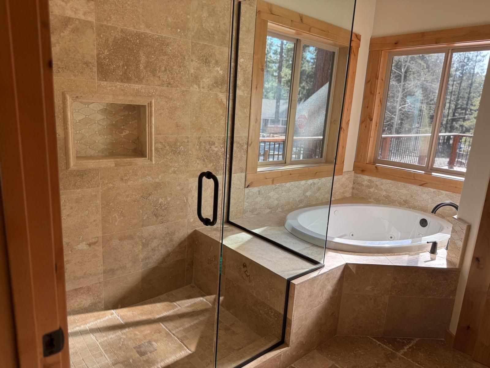 Bathroom with beige tile, glass shower, built-in tub, and windows with outdoor view.