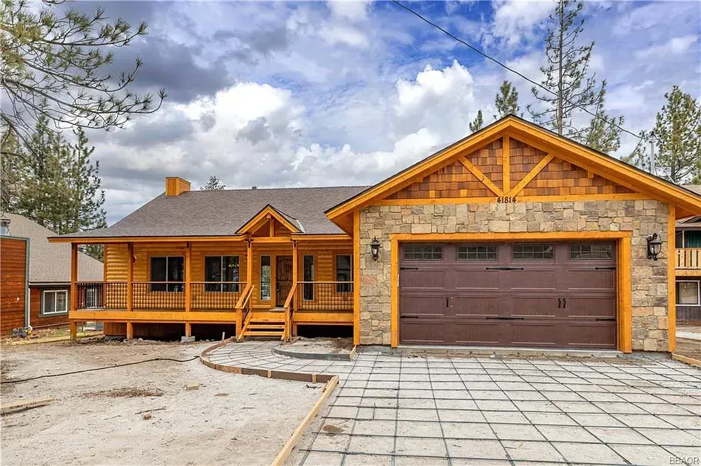 Wooden cabin with stone garage, brown garage door, and a paved driveway.
