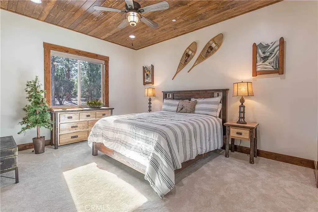 Bedroom with wooden bed frame, dresser, and ceiling. Features neutral color scheme, snowshoes on wall.