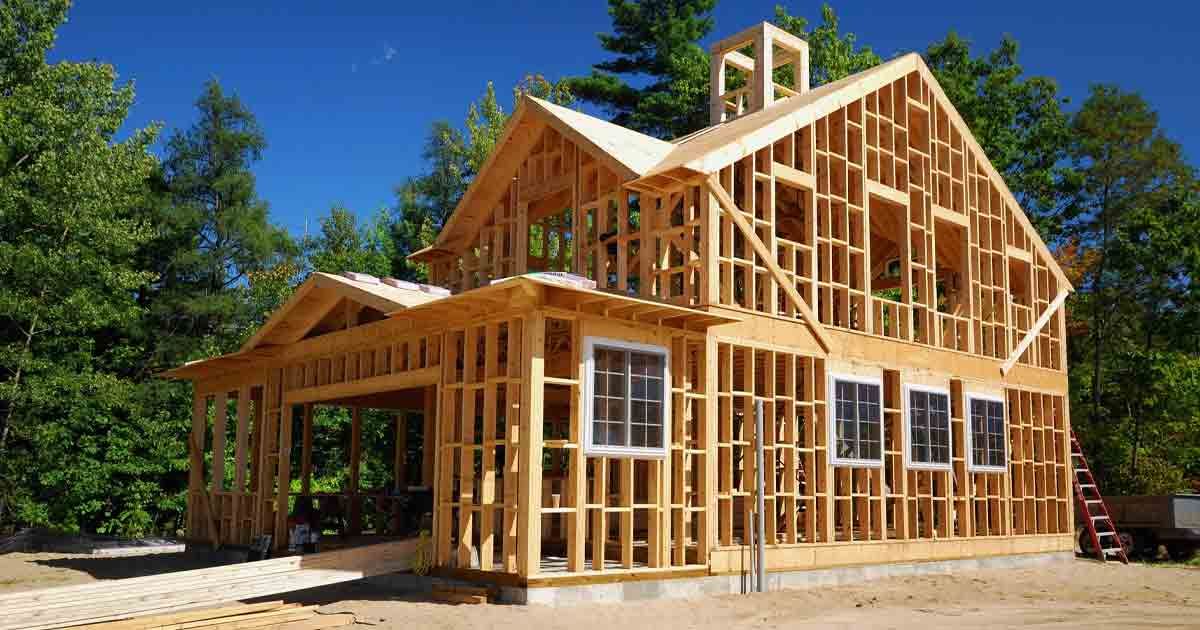 Wood frame of a house under construction; blue sky, trees in the background.
