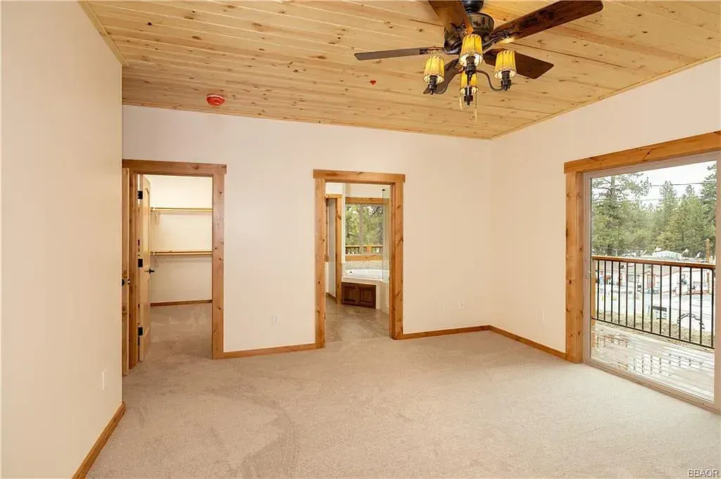 Empty bedroom with wooden ceiling and trim, beige carpet, and sliding door to balcony.