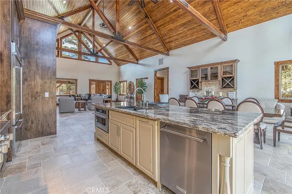 Kitchen with vaulted wood ceiling, stone floor, large island with stainless steel appliances, and adjacent dining area.
