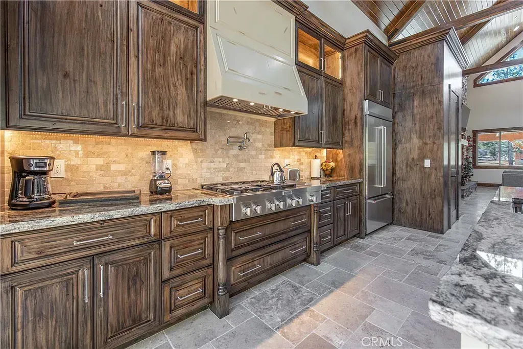 Dark wood kitchen with stainless steel appliances, granite countertops, and stone flooring.
