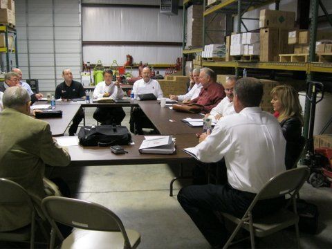 A group of people are sitting around a table in a warehouse
