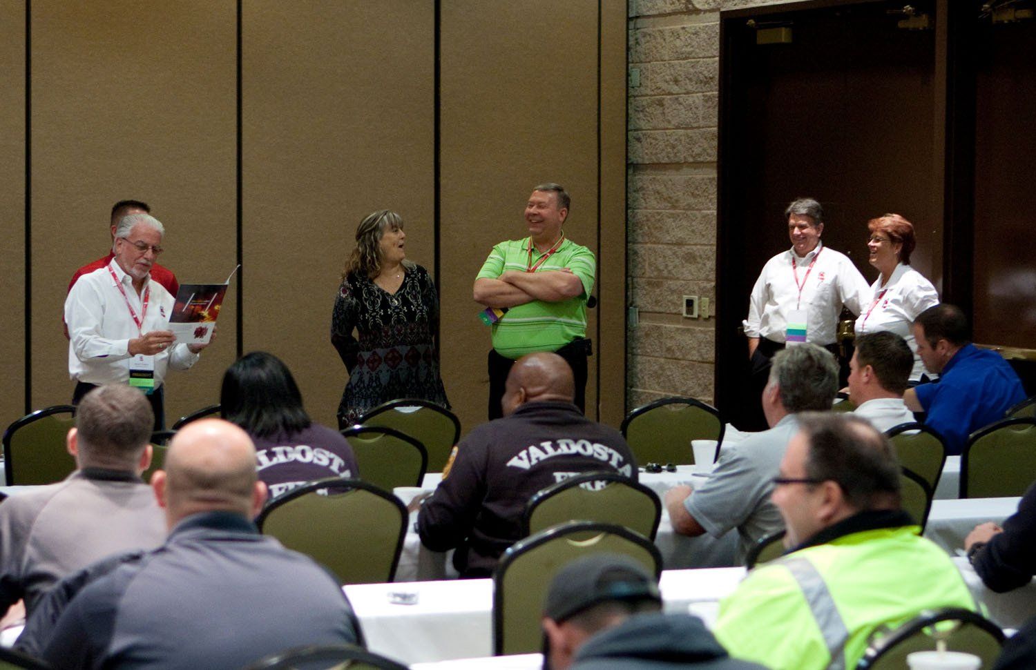 A group of people are sitting at tables with a man wearing a shirt that says valdosta