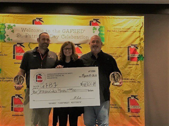 Three people are holding a large check in front of a fire extinguisher wall.