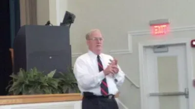 A man in a white shirt and tie is standing in front of a podium.