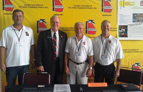 A group of men are standing in front of a yellow wall with fire extinguishers on it.