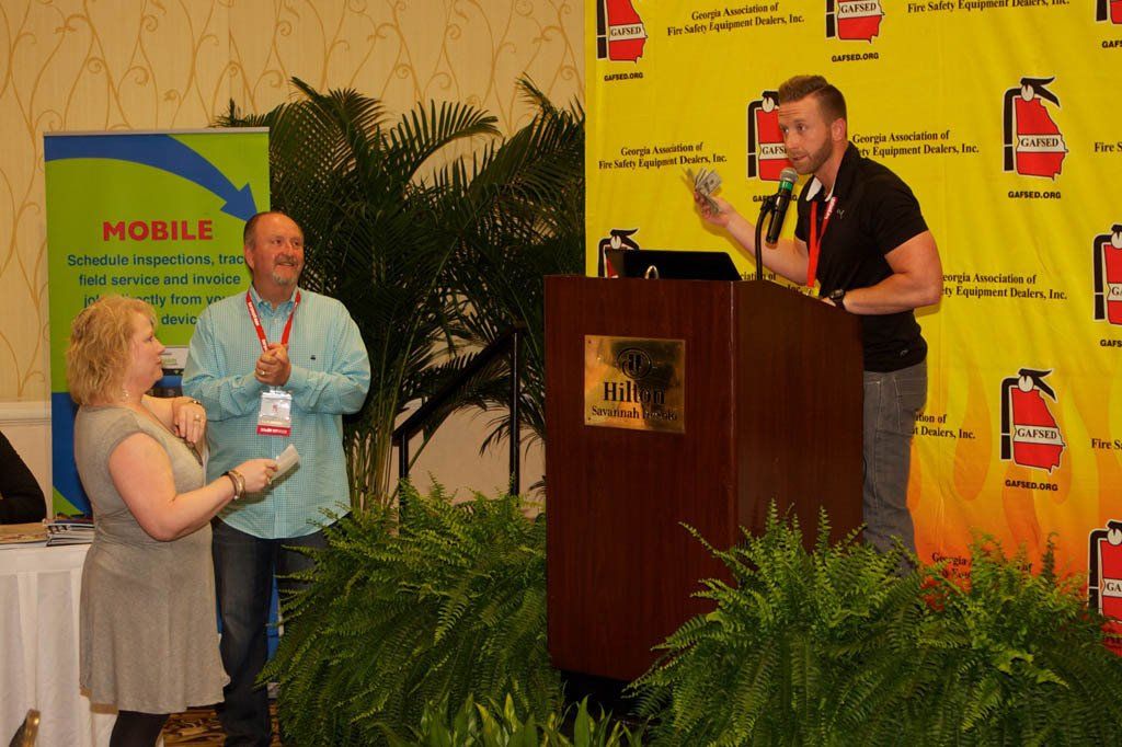 A man stands behind a podium with a fire extinguisher on the wall behind him