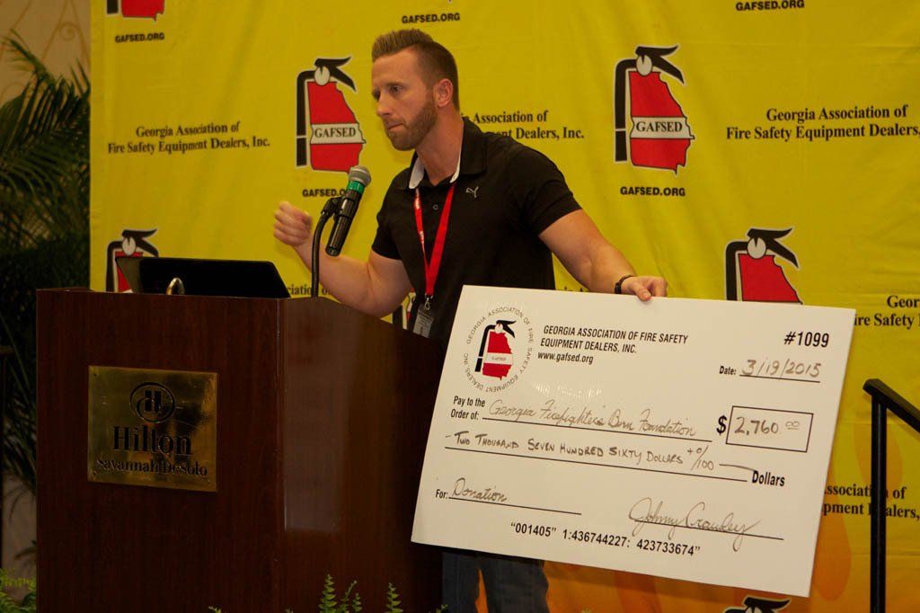 A man stands at a podium holding a large check