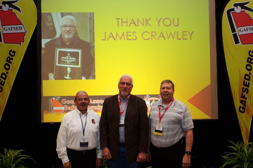 Three men standing in front of a screen that says thank you james crawley