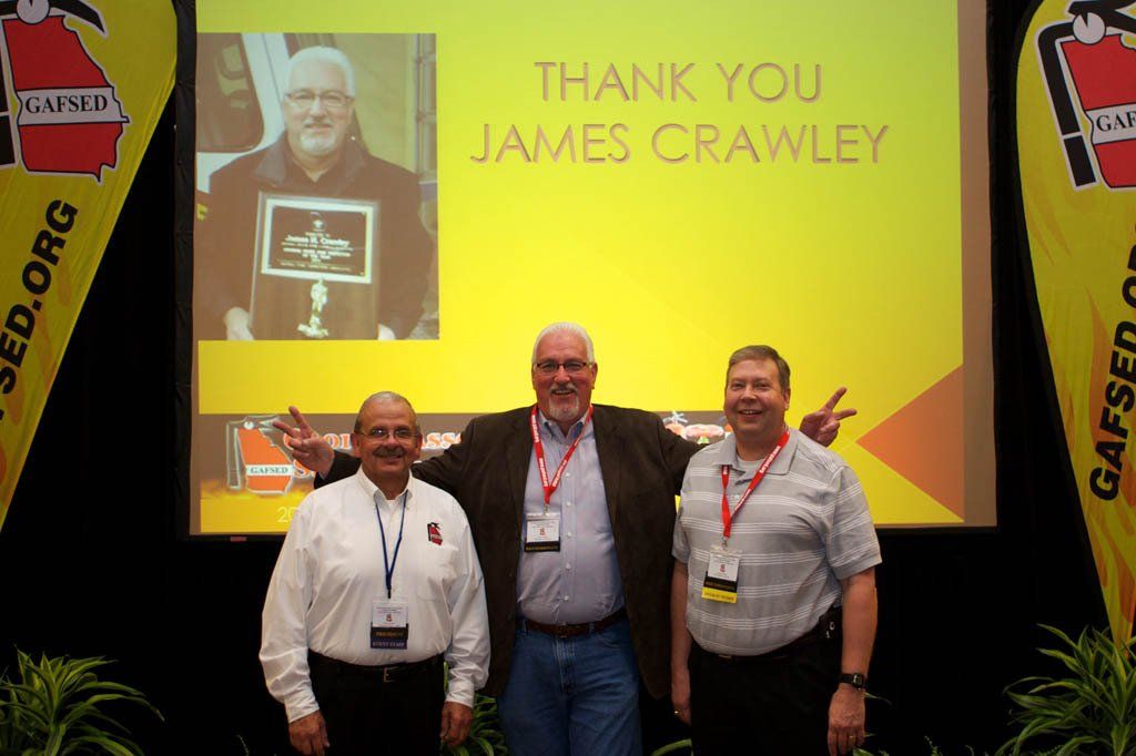 Three men are standing in front of a screen that says thank you james crawley